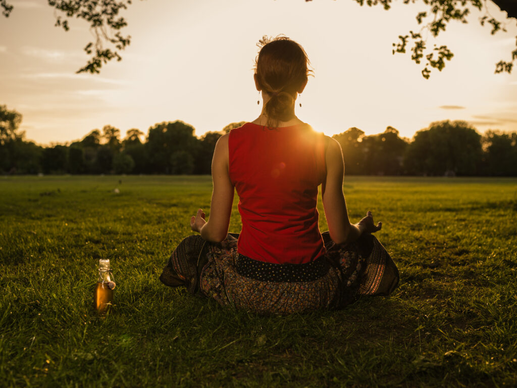 Frau meditiert im Park bei Sonnenaufgang