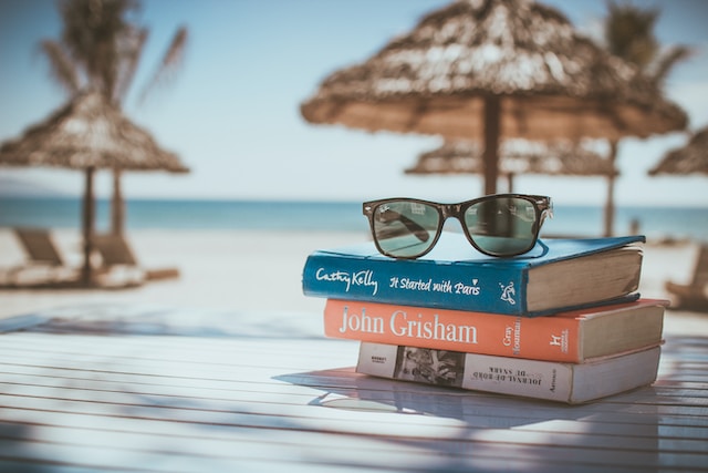 Urlaubslektüre: Sonnenbrille liegt auf Stapel Bücher am Strand