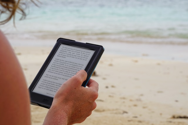 Bücher für den Urlaub: Frau liest mit E-Reader am Strand